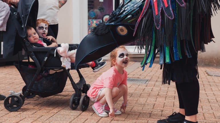 A child in facepiant looking at a giant costume of a crow during Ryde Children's carnival 2022